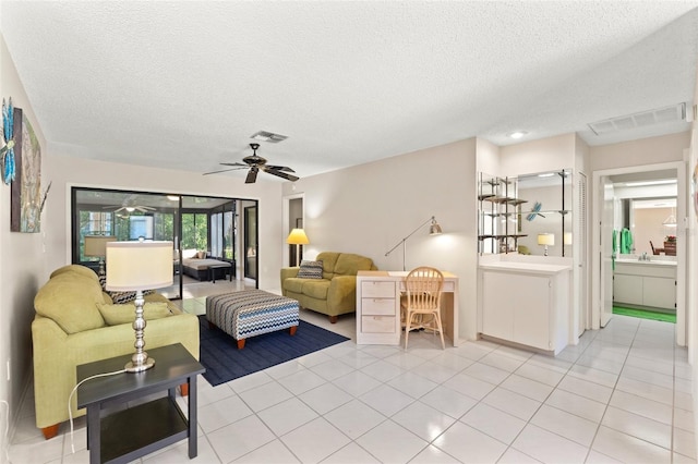 living room with light tile patterned flooring, visible vents, a textured ceiling, and ceiling fan