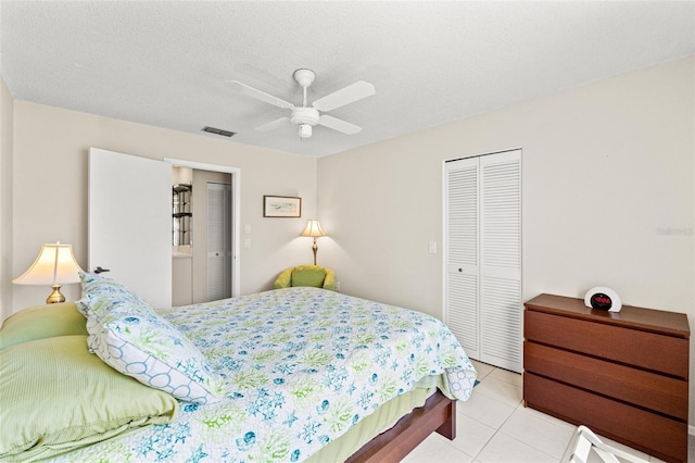 bedroom featuring a ceiling fan, visible vents, light tile patterned flooring, a closet, and a textured ceiling