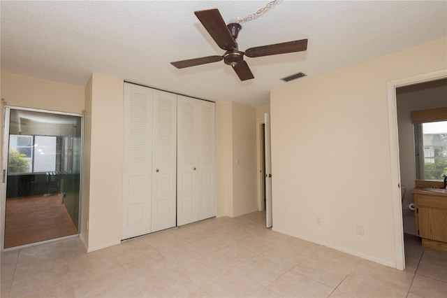unfurnished bedroom featuring visible vents, connected bathroom, light tile patterned floors, a closet, and a textured ceiling