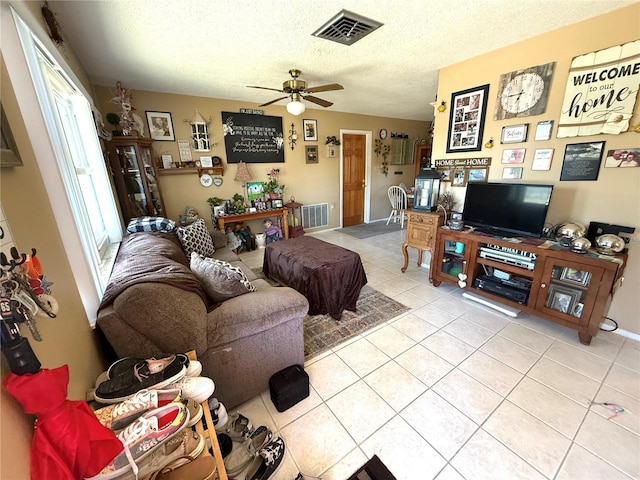 living area featuring light tile patterned flooring, visible vents, a textured ceiling, and a ceiling fan