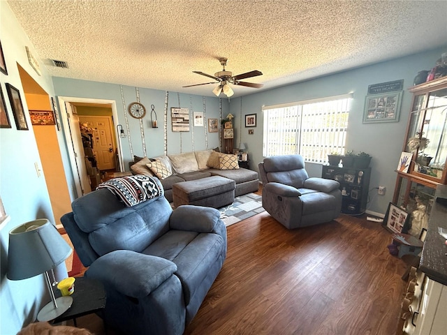 living area with visible vents, baseboards, ceiling fan, wood finished floors, and a textured ceiling