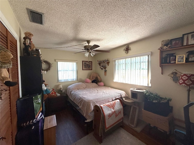 bedroom with visible vents, a textured ceiling, wood finished floors, and a ceiling fan