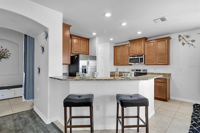 11895 Crestridge Loop, New Port Richey, FL 34655 - kitchen with a breakfast bar area, stainless steel appliances, visible vents, a peninsula, and brown cabinets