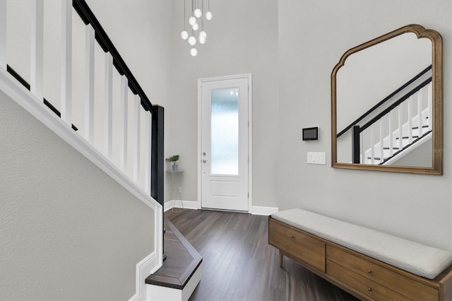 entryway with dark wood finished floors, stairway, a towering ceiling, and baseboards