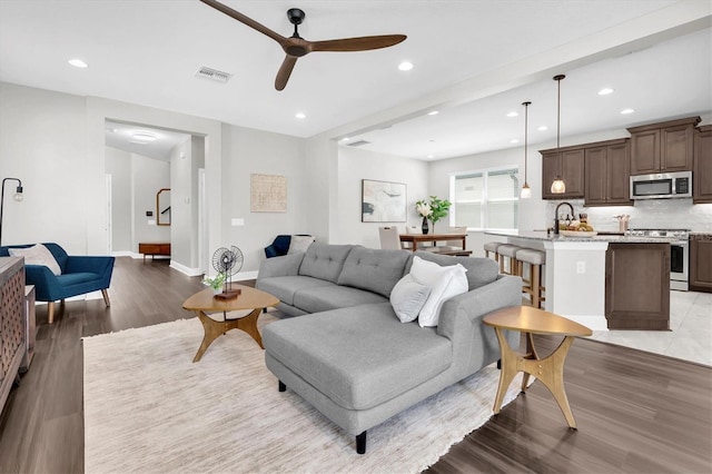 living area featuring a ceiling fan, wood finished floors, baseboards, visible vents, and recessed lighting