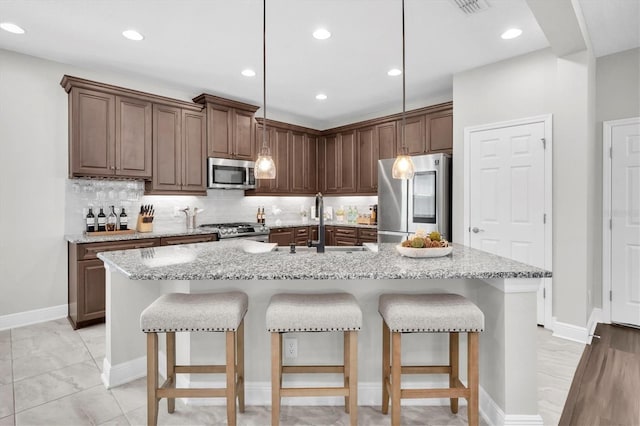 kitchen with light stone counters, a kitchen breakfast bar, tasteful backsplash, a sink, and appliances with stainless steel finishes