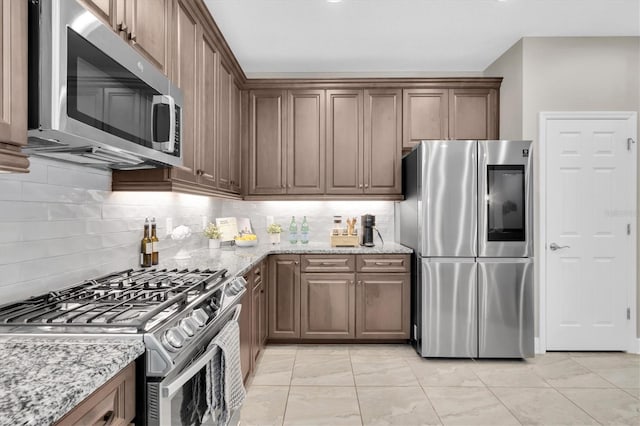 kitchen featuring backsplash, appliances with stainless steel finishes, and light stone counters