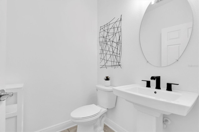 half bath featuring toilet, baseboards, and a sink
