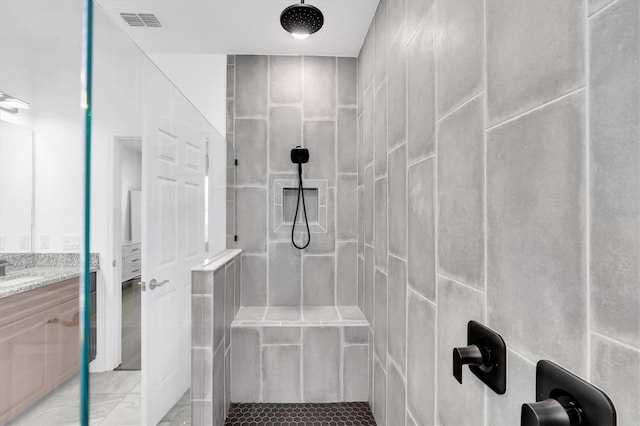 full bathroom featuring a tile shower, vanity, and visible vents