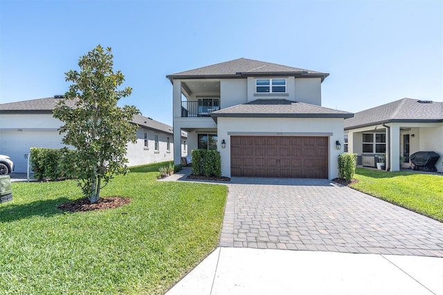 view of front facade featuring a balcony, stucco siding, decorative driveway, a front yard, and a garage