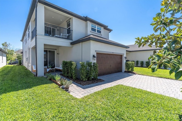 view of front facade featuring driveway, a balcony, a front yard, and stucco siding