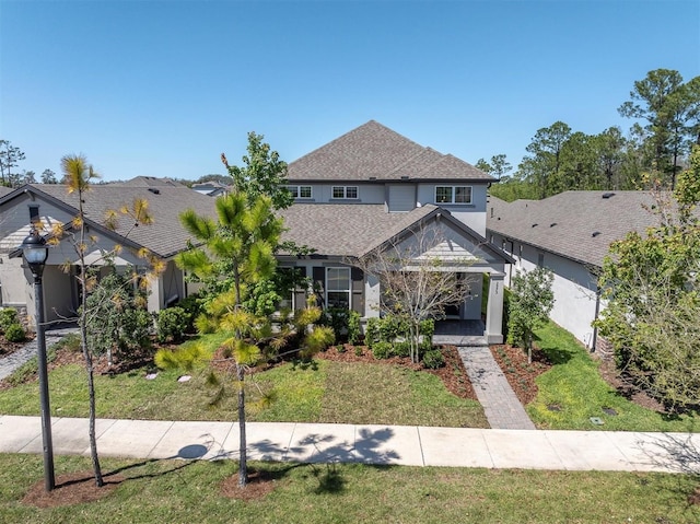 view of front facade featuring a shingled roof, a front lawn, and stucco siding