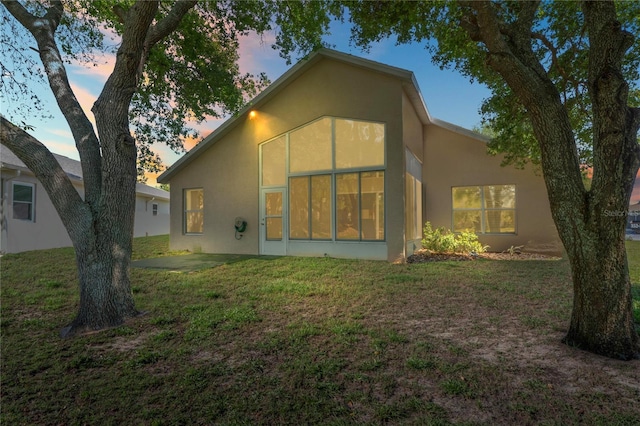 303 Rochester St, Spring Hill, FL 34609 - back of property at dusk with stucco siding, a lawn, and a sunroom