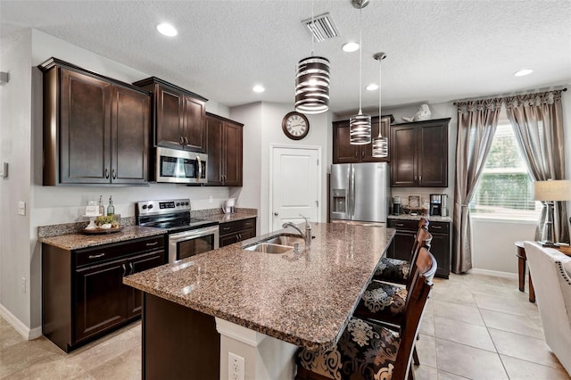 kitchen with visible vents, stone countertops, a sink, stainless steel appliances, and dark brown cabinets