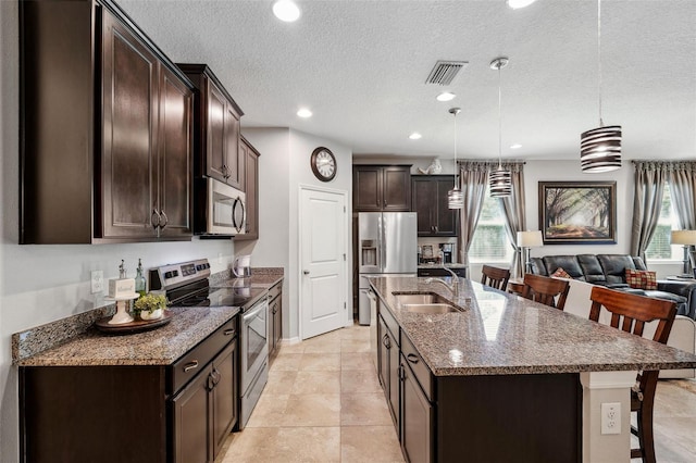 kitchen with visible vents, a sink, appliances with stainless steel finishes, a breakfast bar area, and dark brown cabinets