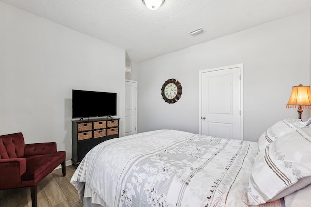 bedroom with wood finished floors, visible vents, and a textured ceiling
