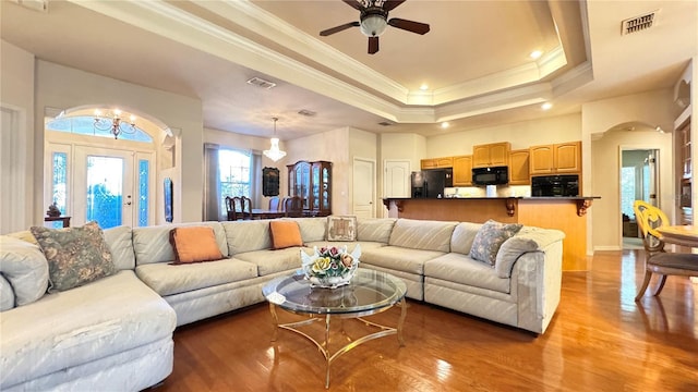 living room featuring a tray ceiling, ornamental molding, ceiling fan with notable chandelier, visible vents, and light wood-style flooring