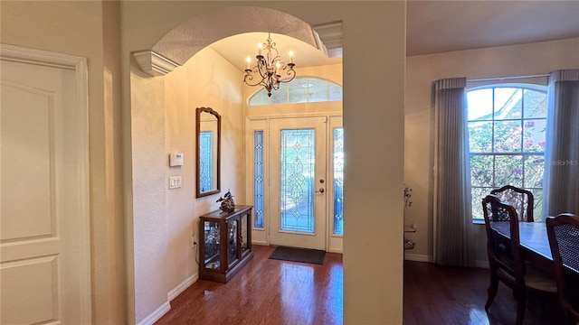 foyer with baseboards, arched walkways, wood finished floors, and a chandelier