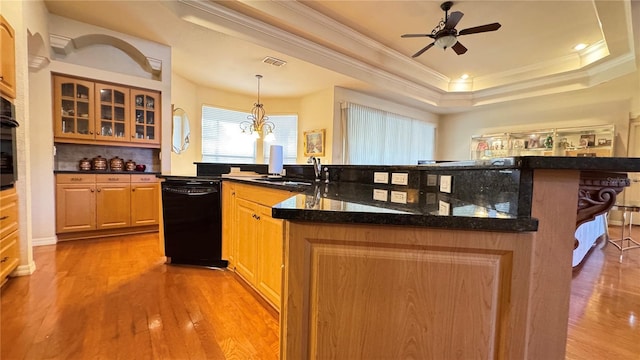 kitchen featuring visible vents, light wood-style flooring, a breakfast bar area, a tray ceiling, and black appliances