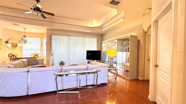 living room featuring crown molding, dark wood-style flooring, ceiling fan with notable chandelier, a raised ceiling, and visible vents
