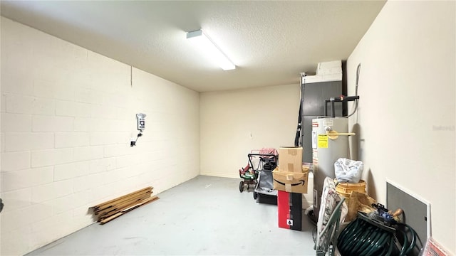 finished basement with concrete block wall, water heater, and a textured ceiling