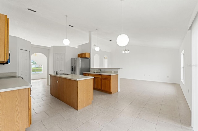 kitchen with stainless steel refrigerator with ice dispenser, arched walkways, brown cabinets, vaulted ceiling, and light countertops