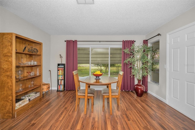 dining space with baseboards, a textured ceiling, wood finished floors, and visible vents