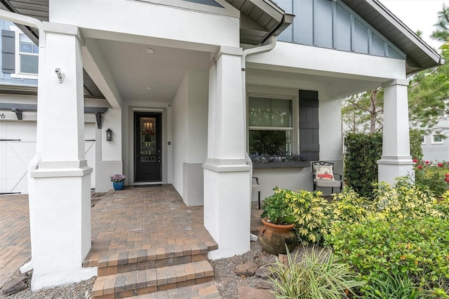 view of exterior entry with stucco siding, a porch, board and batten siding, and a garage