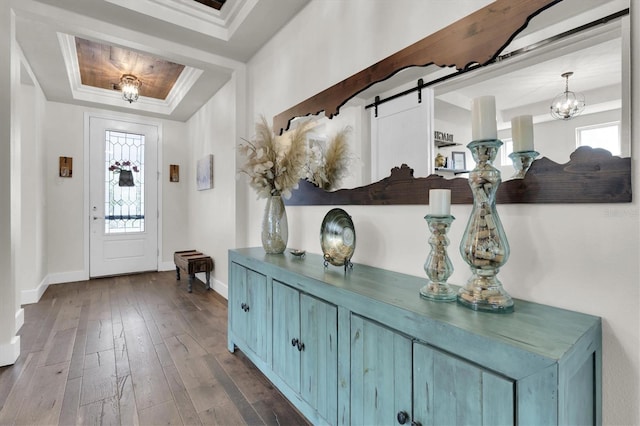 foyer entrance featuring a tray ceiling, dark wood-style floors, baseboards, ornamental molding, and an inviting chandelier