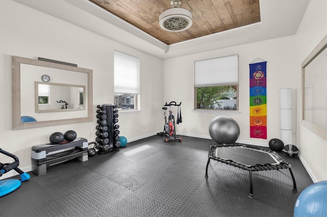 exercise room with wood ceiling, a tray ceiling, and baseboards