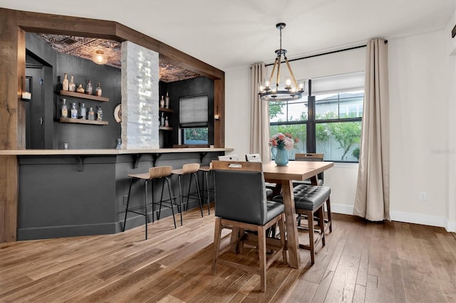 dining area featuring a notable chandelier, a dry bar, baseboards, and wood finished floors