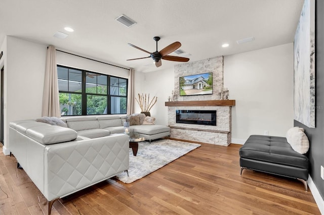 living area with wood finished floors, ceiling fan, a fireplace, and visible vents