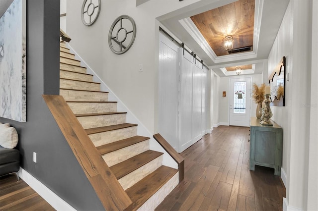 entrance foyer with crown molding, hardwood / wood-style flooring, stairs, a barn door, and a tray ceiling