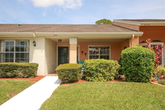 9321 Whitstone Ct, New Port Richey, FL 34655 - entrance to property with roof with shingles, brick siding, and a yard