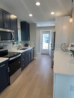 kitchen featuring light countertops, backsplash, pendant lighting, stainless steel appliances, and light wood-style floors