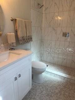 bathroom featuring toilet, vanity, tile patterned floors, and tiled shower