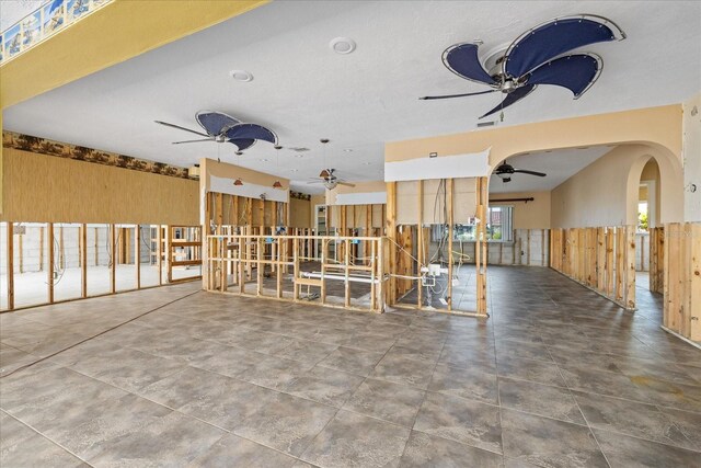 5000 Southshore Dr, New Port Richey, FL 34652 - unfurnished living room featuring ceiling fan, wood walls, a wainscoted wall, and arched walkways