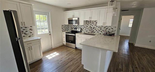 807 S Castle Ct, Tampa, FL 33612 - kitchen with white cabinetry, dark wood finished floors, a sink, a peninsula, and appliances with stainless steel finishes