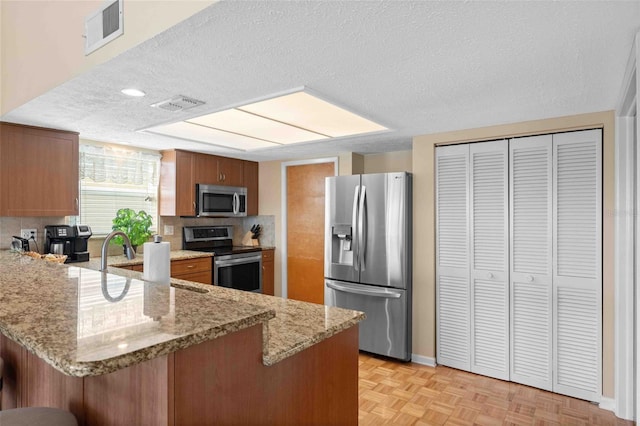 4058 Centavo Ct, Hernando Beach, FL 34607 - kitchen with stainless steel appliances, a peninsula, a textured ceiling, brown cabinetry, and a breakfast bar area