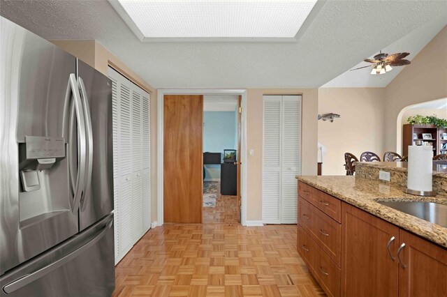 4058 Centavo Ct, Hernando Beach, FL 34607 - kitchen with stainless steel fridge with ice dispenser, brown cabinetry, a ceiling fan, light stone counters, and baseboards