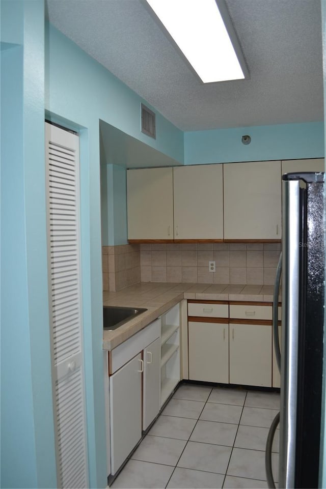 kitchen featuring freestanding refrigerator, tasteful backsplash, light tile patterned flooring, tile counters, and a sink