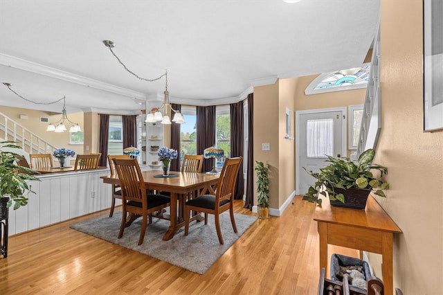 dining area with light wood finished floors, baseboards, ornamental molding, and an inviting chandelier