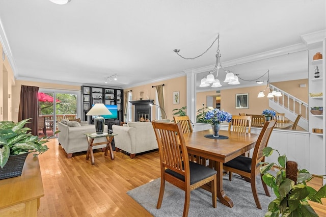 dining area featuring light wood-type flooring, crown molding, a lit fireplace, and a chandelier