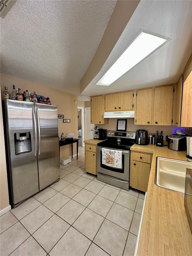 kitchen featuring a sink, under cabinet range hood, light countertops, light tile patterned floors, and appliances with stainless steel finishes
