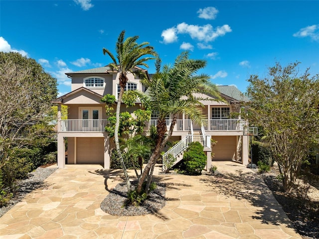 coastal home featuring concrete driveway, stucco siding, stairway, an attached garage, and a porch