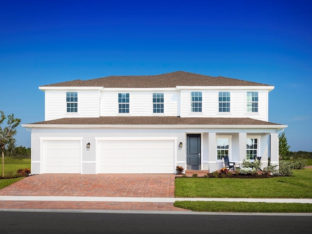 view of front of property featuring roof with shingles, decorative driveway, a front yard, covered porch, and a garage