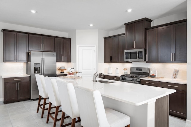 kitchen featuring a kitchen bar, a sink, dark brown cabinetry, and appliances with stainless steel finishes