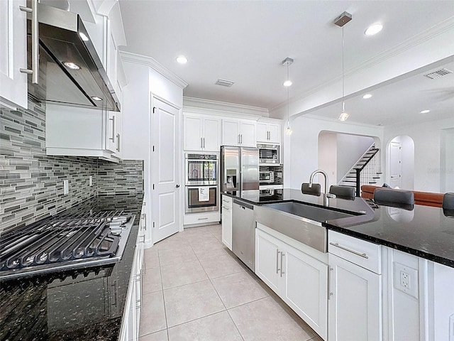 kitchen featuring visible vents, arched walkways, a sink, stainless steel appliances, and wall chimney exhaust hood