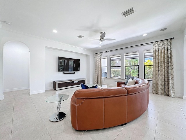 living area featuring arched walkways, a ceiling fan, light tile patterned floors, visible vents, and ornamental molding