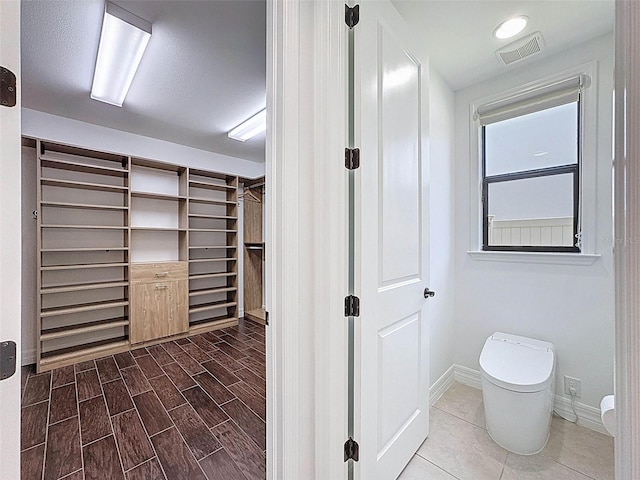 interior space with a walk in closet, visible vents, wood finished floors, baseboards, and toilet